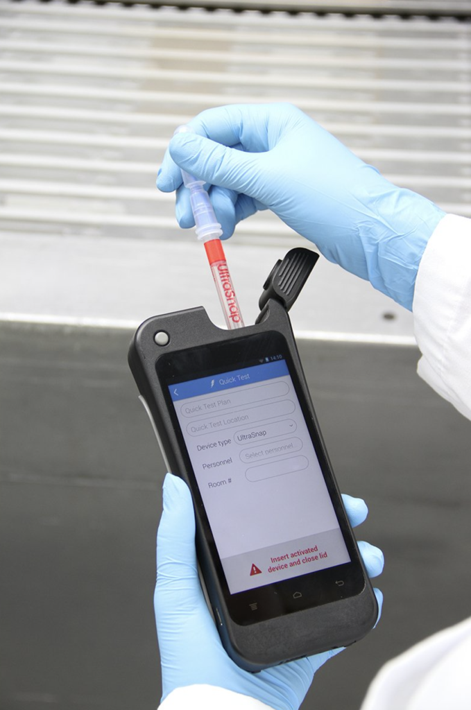 Gloved hands inserting test tube into handheld analyzer