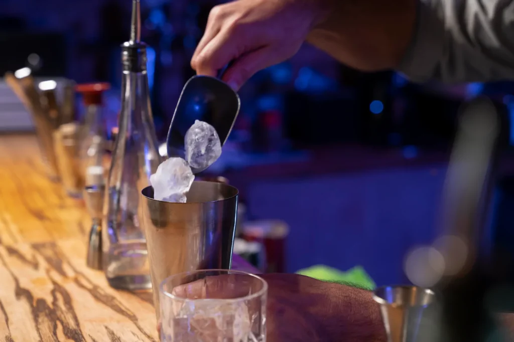 Bartender adding ice to cocktail shaker at bar